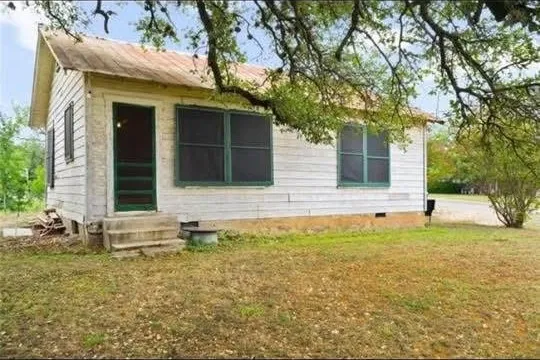 The same cottage before work, with peeling white siding, green window frames and a bare concrete step