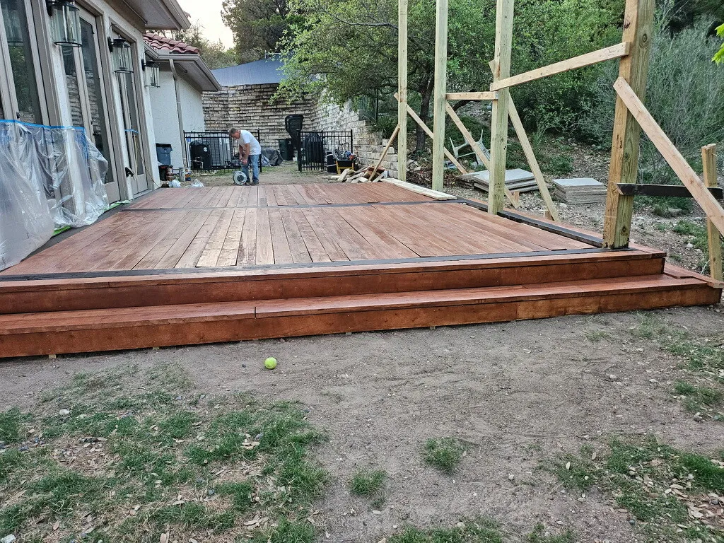 Deck boards stained and sealed with the patio cover posts going up behind them