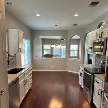 Kitchen with white painted cabinets, dark wood floors and arched windows at the breakfast nook