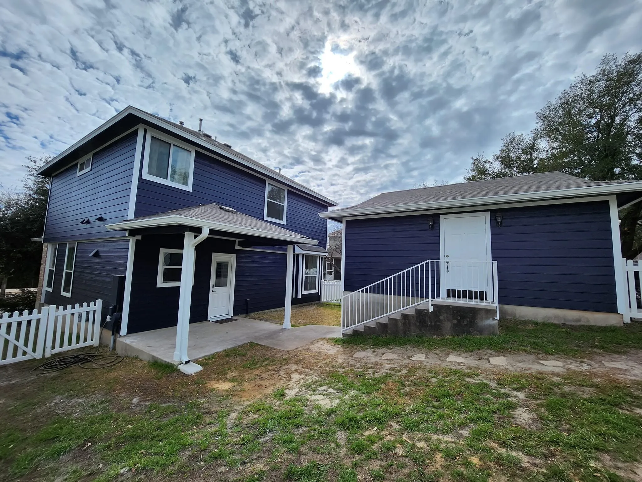 Two-story navy blue home with white trim and a white porch rail under a dramatic cloudy sky