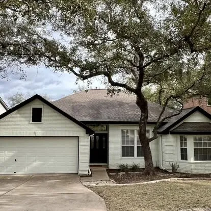 White painted brick home with black trim and a black front door under a large live oak