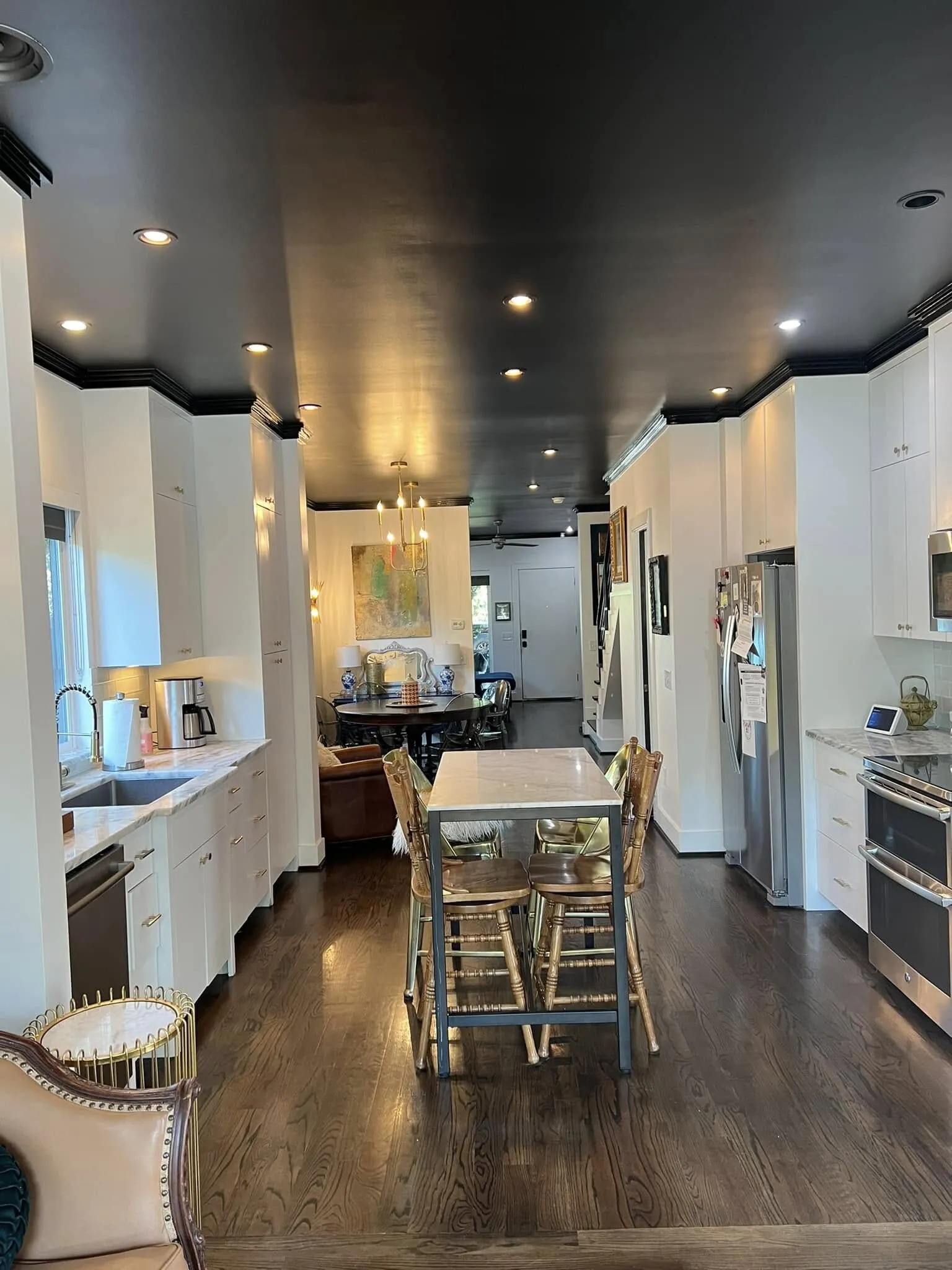 Open kitchen with white cabinets, an island with bar stools and a dark charcoal ceiling